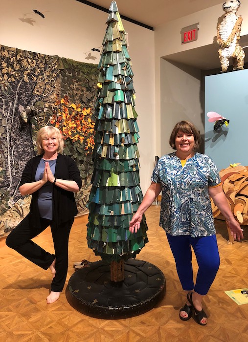 two women tree posing by a tree sculpture